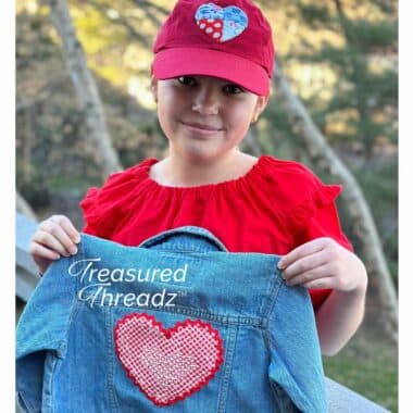 Model wearing hat and holding upcycled jean jacket made with Heart to Art Applique pattern featuring Treasured Threadz Postage Stamp Retro Fabric Panel